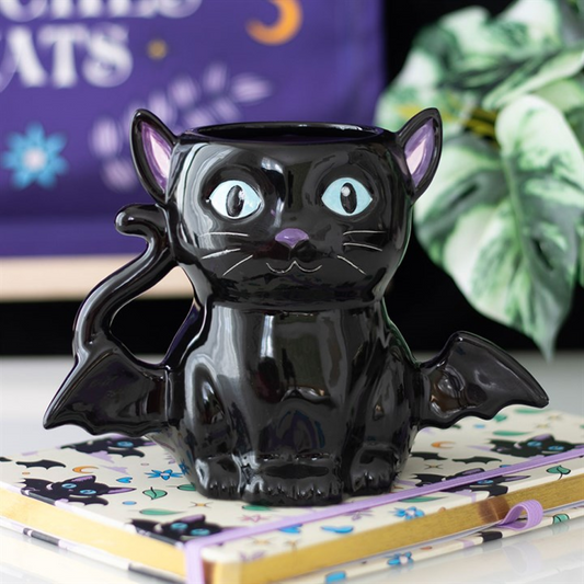Black cat-shaped mug with bat wings on a notebook